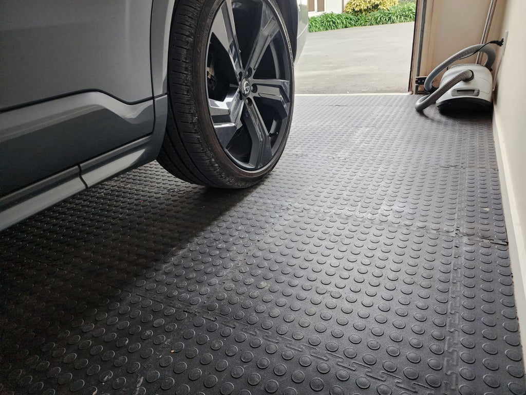 Car wheel on a textured black garage tile with a vehicle partially visible.
