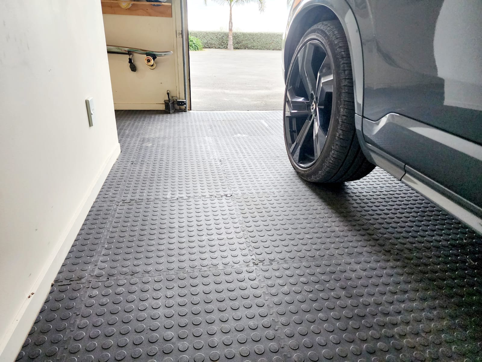 Car parked on a textured black garage floor tiles in front of an open garage door.