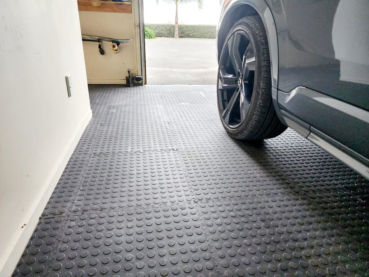 Car parked on a textured black garage floor tiles in front of an open garage door.