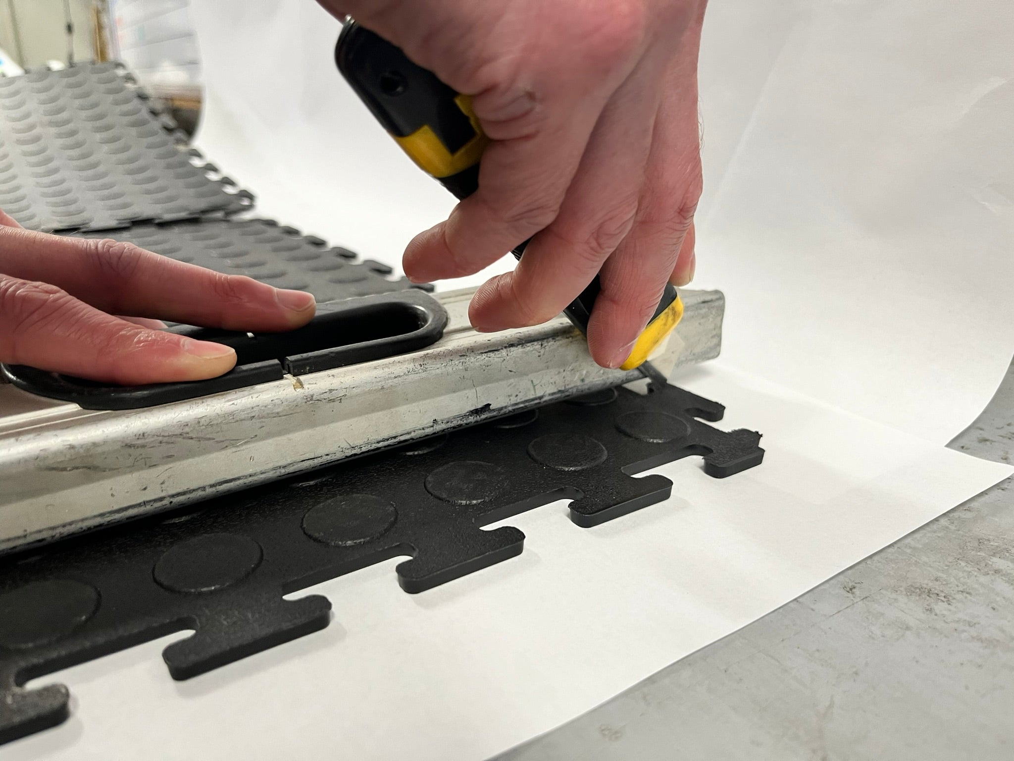 Cutting a garage floor tile with a utility knife along a straight edge, easy DIY install