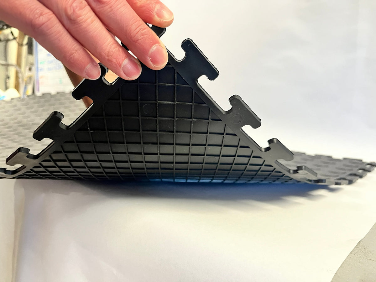 Hand bending a black garage floor tile to demonstrate its flexibility